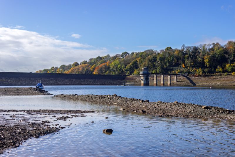 The scale of Llandegfedd's dam wall and intake tower against a dramatically low water level with exposed gravel banks, usually submerged, starkly illustrate the UK's significant water supply challenge